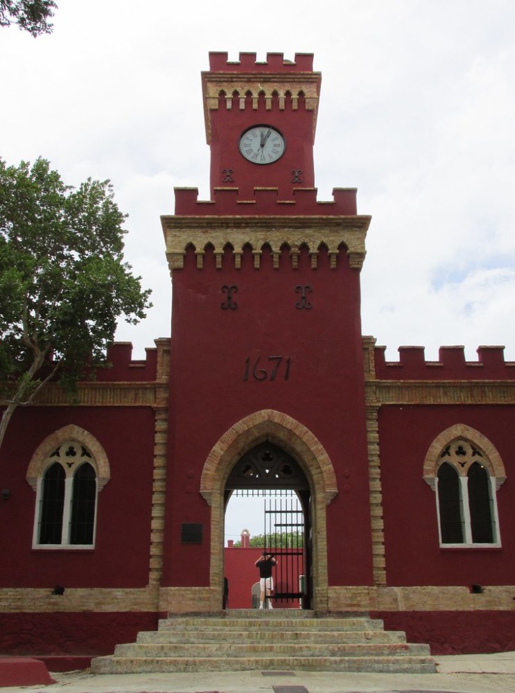 a large stone building with a clock tower with Fort Christian in the background